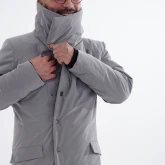 Мужчина застёгивает длинное светло-серое зимнее пальто на кнопках