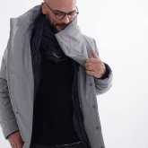 Мужчина показывает внутреннюю сторону длинного светло-серого зимнего пальто