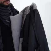 Мужчина держит в руках длинное светло-серое зимнее пальто на кнопках