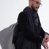 Мужчина несёт на плече длинное светло-серое зимнее пальто