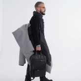 Мужчина идёт с длинным светло-серым зимним пальто на плече и сумкой в руке