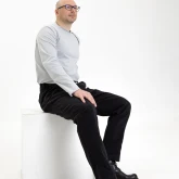 Мужчина в черных джинсовых брюках, сидит на кубе, вид сбоку