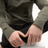 Асимметричная зеленая футболка с длинным рукавом, модель сидит, вид рукава и низа изделия