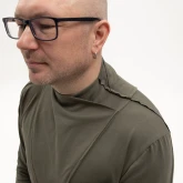 Асимметричная зеленая футболка с длинным рукавом, модель в очках в полубоком ракурсе